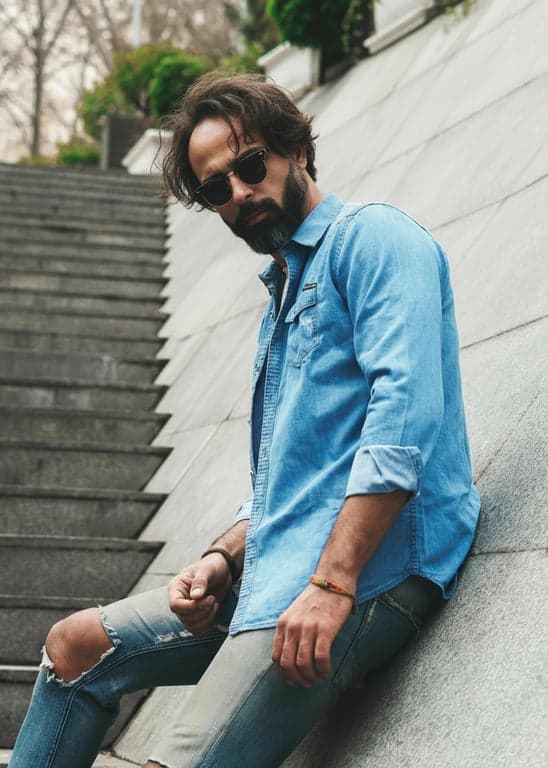 a portrait of a person enhanced for thicker hair appearance by reinforcing hair density at the crown and mid-lengths; keep original silhouette and hairline intact; avoid inflated or wig-like effects; maintain natural hair movement and flyaways; no changes to face, background, or lighting; realistic portrait finish