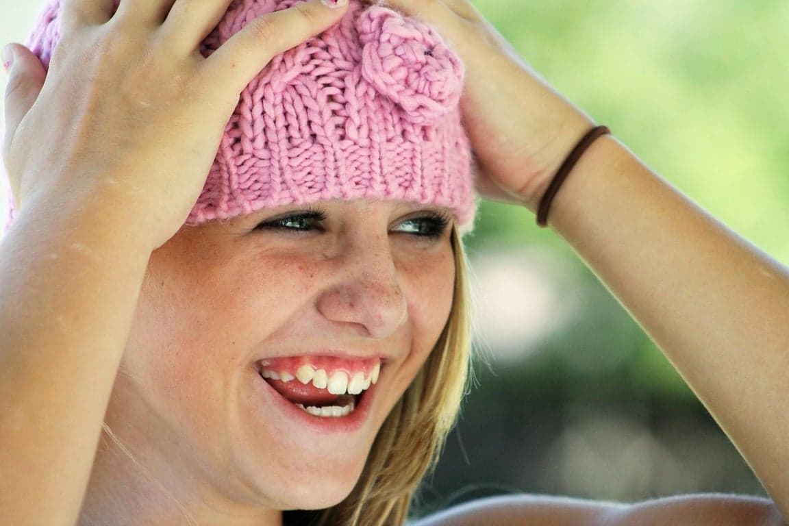 AI teeth whitening filter before photo - woman wearing pink hat smiling in sunlight