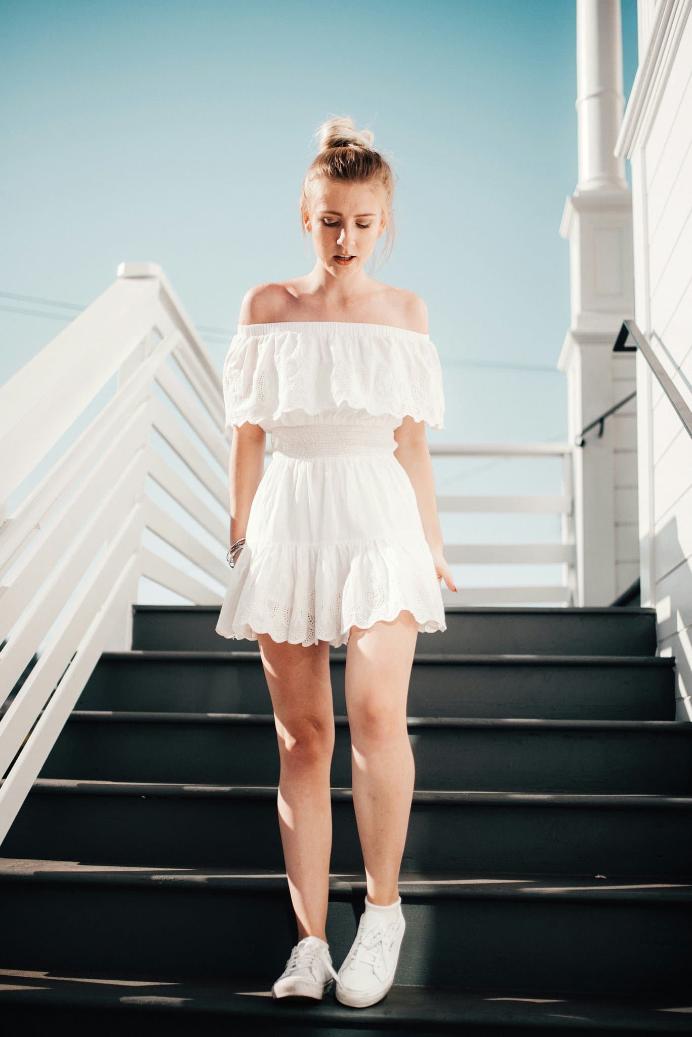 A woman in a white off shoulder dress walking down outdoor stairs.