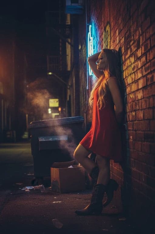 a portrait of a person transformed with an urban neon glow, standing in a dark alley illuminated by the warm glow of nearby neon signs