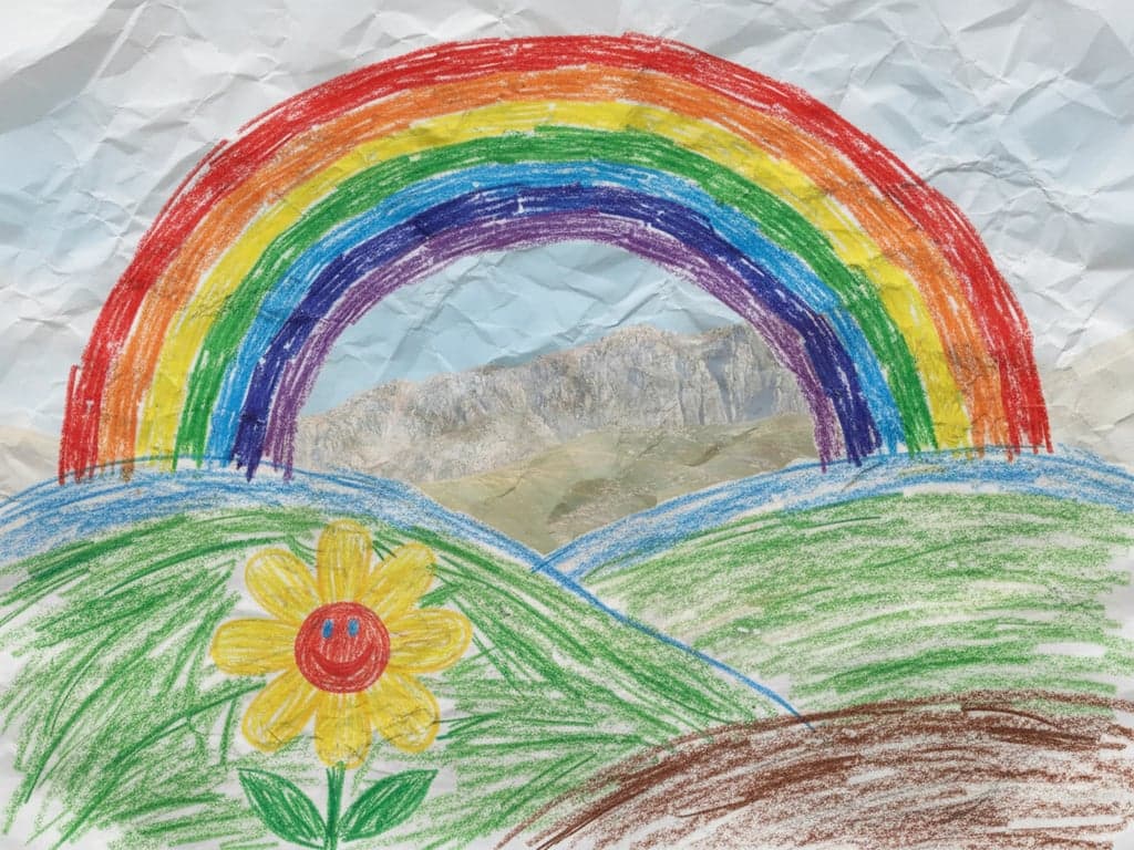 A crayon drawing of a rainbow over hills, with a smiling flower, visible pressure marks from the crayon, colors layered messily, on crinkled paper.