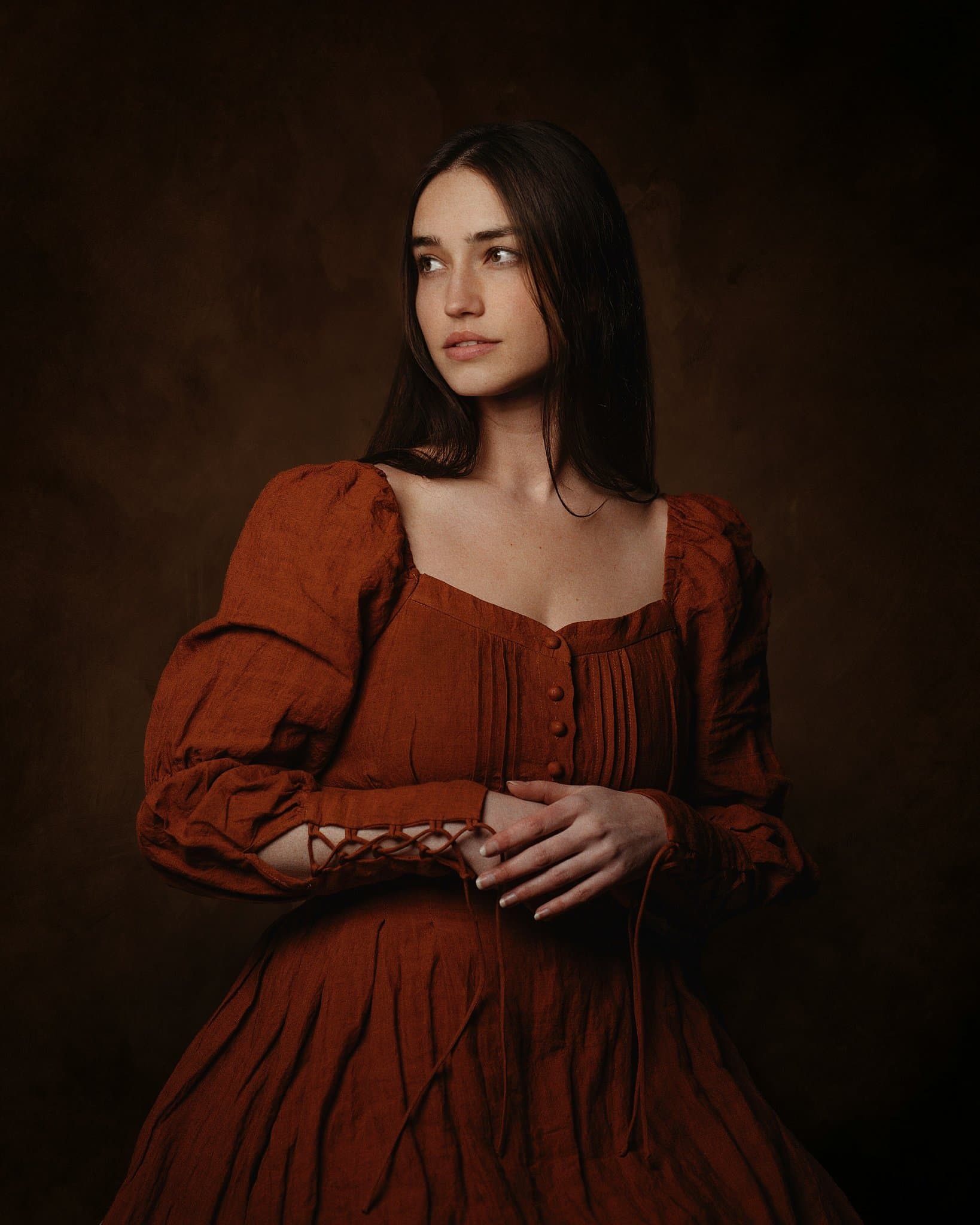 The subject wears a textured brown dress with historical styling and long sleeves.