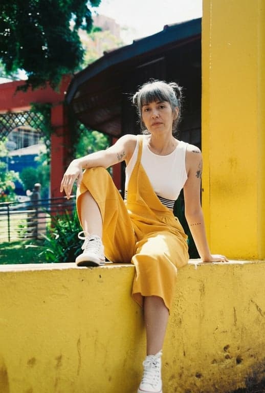 age ai generator after photo - woman sitting on the yellow wall in her 60s