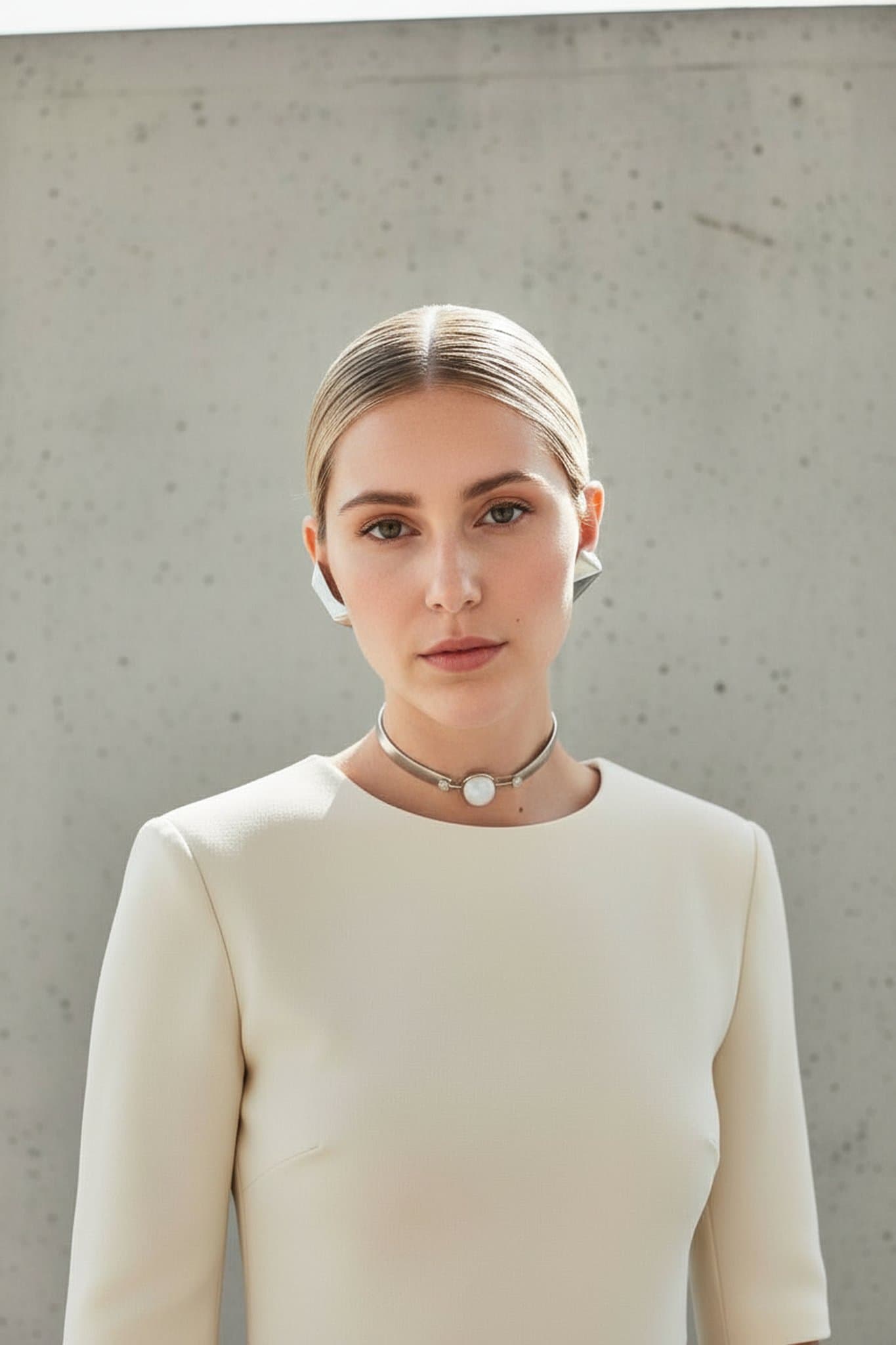 Minimalist cream dress, sleek hairstyle, metallic choker, neutral concrete background, calm facial expression.