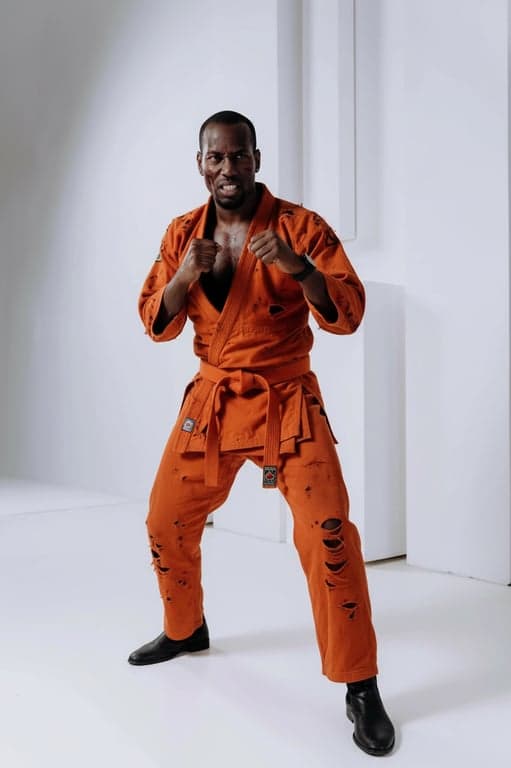 a portrait of a person wearing a torn orange martial arts gi (dogi), with scuffs and bruises, in a determined fighting stance