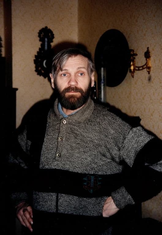 a portrait of a man with a classic goatee style, featuring a neatly trimmed beard on the chin and a mustache, against a solid background