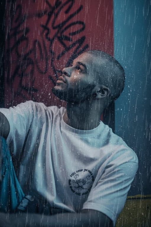 A cinematic sad edit of a man in the rain, with filter-adding rain streaks and tears blending together, cool blue tone, low saturation, poignant mood.